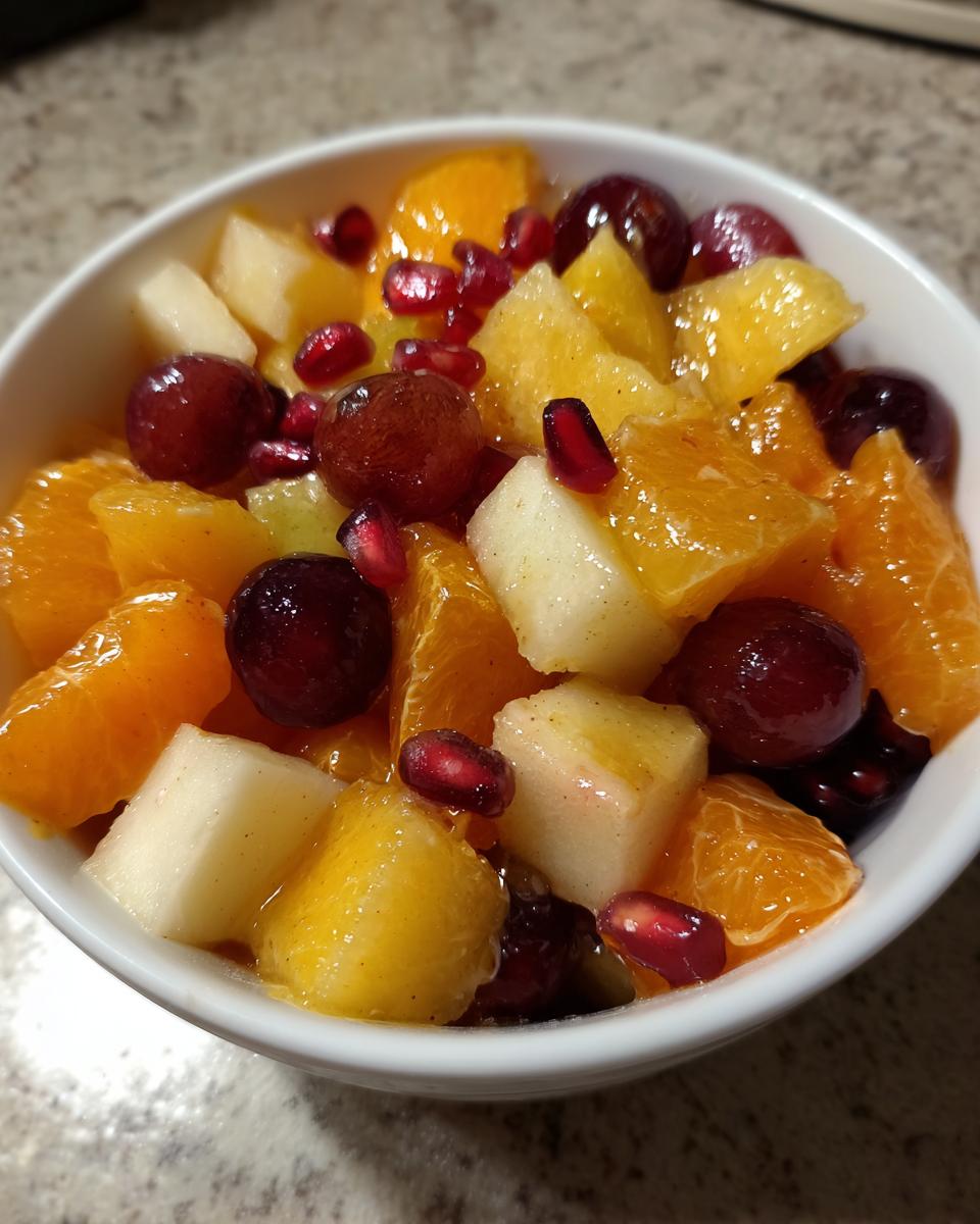 A close-up of a vibrant winter fruit salad featuring oranges, grapes, pears, and pomegranate seeds in a white bowl.