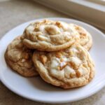 A stack of four gooey white chocolate macadamia nut cookies resting on a small white plate.