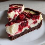 Close-up of a rich white chocolate raspberry cheesecake slice with a dark crust and raspberry swirl.