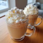 Two glass mugs filled with creamy white hot chocolate, topped high with whipped cream and mini marshmallows.