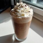 A tall glass filled with blended frozen hot chocolate, topped with whipped cream and chocolate shavings.
