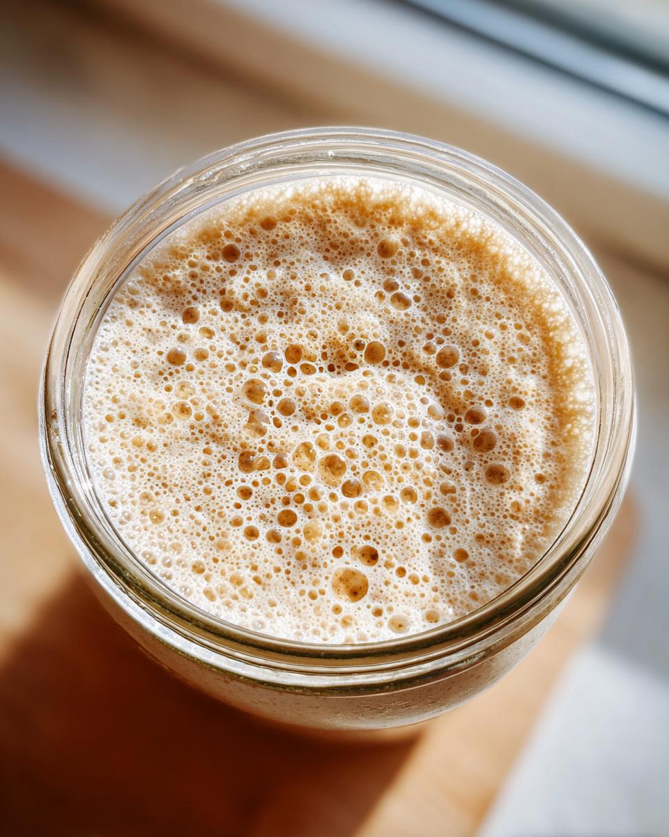 Overhead view of an active sourdough starter showing many small, active bubbles in a glass jar.