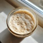 Overhead view of a very active sourdough starter in a glass jar, showing lots of bubbles and foam.