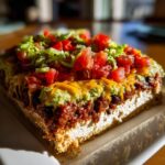 A cross-section slice of a rich, multi-layered 7 layer dip showing cream cheese, taco meat, guacamole, cheese, lettuce, and tomatoes.