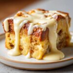 Close-up of a moist slice of bread pudding topped generously with rich vanilla sauce.
