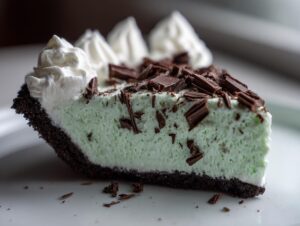 Close-up of a slice of bright green grasshopper pie with a dark chocolate crust, topped with whipped cream and chocolate shavings.