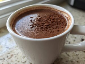 Close-up of a steaming mug filled with rich, dark hot cocoa mix, topped with cocoa powder.