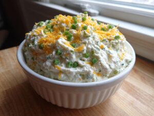 A creamy bowl of amazing 10-minute pickle dip topped with shredded cheddar cheese and green onions.