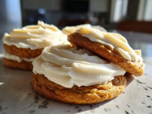 Close-up of soft pumpkin cookie sandwiches filled and topped with thick cream cheese frosting.