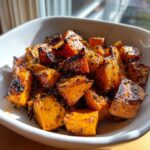 Close-up of caramelized, seasoned roasted sweet potatoes cubes served in a white bowl.