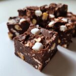 A close-up of rich, dark chocolate rocky road fudge squares studded with marshmallows and nuts.