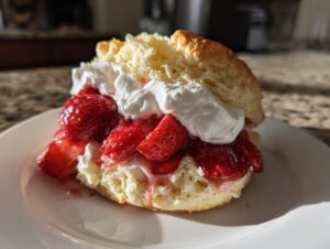 Close-up of a fluffy biscuit shortcake filled with macerated strawberries and whipped cream.