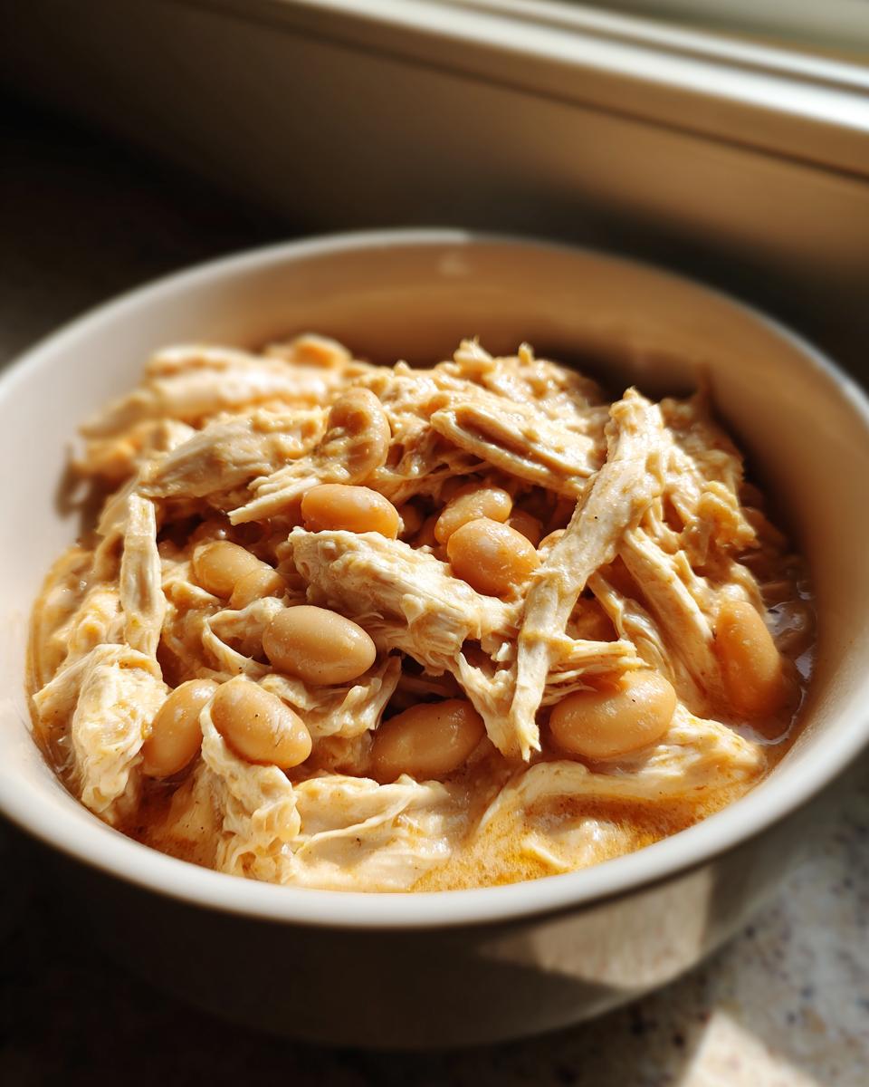 A close-up shot of a bowl filled with creamy, shredded chicken and white beans, representing cream cheese chicken chili.