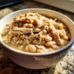 Close-up of a white bowl filled with rich, creamy cream cheese chicken chili featuring shredded chicken and white beans.