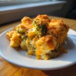 A close-up serving of creamy broccoli cauliflower casserole topped with melted cheddar cheese and crispy breadcrumbs.