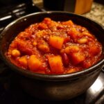 Close-up of a dark bowl filled with thick, rich butternut squash chili, featuring visible chunks of orange squash and beans.
