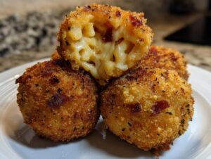 Close-up of crispy, golden-brown fried rice balls, one cut open revealing melted cheese and macaroni filling.