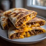 Close up of cheesy pocket tacos cut in half, showing melted cheddar cheese oozing out with savory ground beef filling.