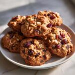 A stack of chewy fruitcake cookies loaded with dried cranberries and nuts, resting on a light plate.