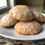 A stack of four chewy lemon cookies topped with a thick white glaze and bright yellow lemon zest.