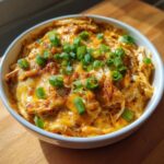Close-up of hot chicken enchilada dip topped with melted orange cheese and fresh green onions.