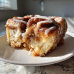 A close-up of a gooey, iced cinnamon roll, representing the cinnamon roll apple pie fusion.