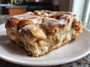 A close-up of a soft, glazed slice of cinnamon roll apple pie showing the swirl and apple filling.