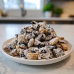 A generous mound of cookies and cream puppy chow coated in powdered sugar on a white plate.