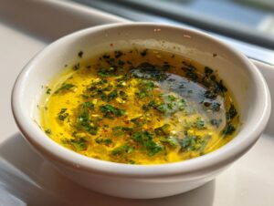 Close-up of melted butter with herbs and spices, showcasing the vibrant cowboy butter dipping sauce in a small white bowl.