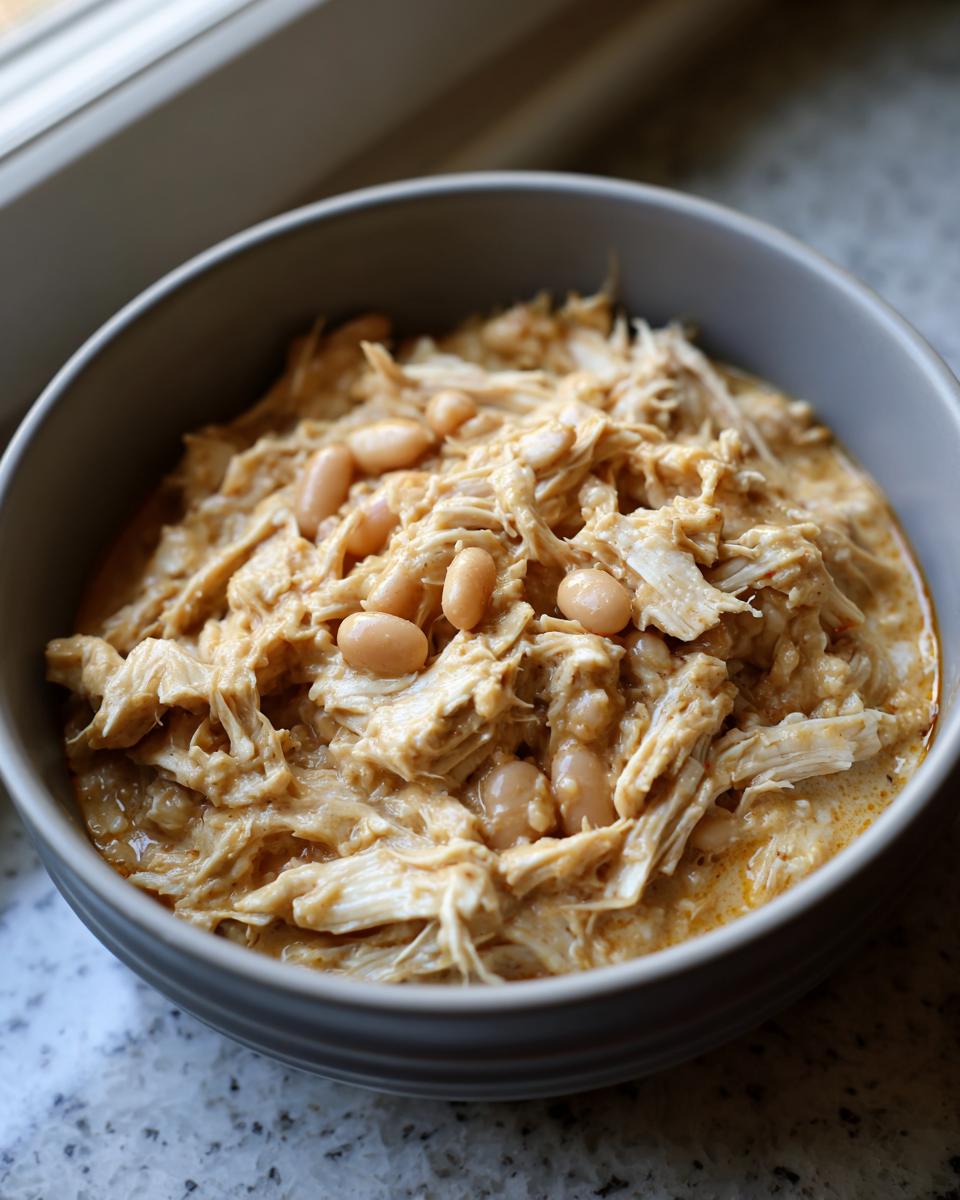 Close-up of a bowl of creamy, shredded cream cheese chicken chili topped with white beans.