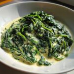 A close-up of a white bowl filled with rich, homemade creamed spinach recipe.