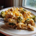 A spoonful of creamy chicken broccoli rice casserole topped with melted cheddar cheese being lifted from a plate.