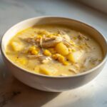A close-up of creamy chicken corn chowder filled with shredded chicken, corn kernels, and potato chunks in a white bowl.