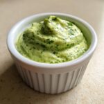 Close-up of thick, bright green cilantro lime sauce swirled high in a small white ramekin.