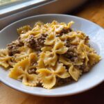 Close-up of creamy parmesan garlic beef bowtie pasta served in a white bowl near a window.