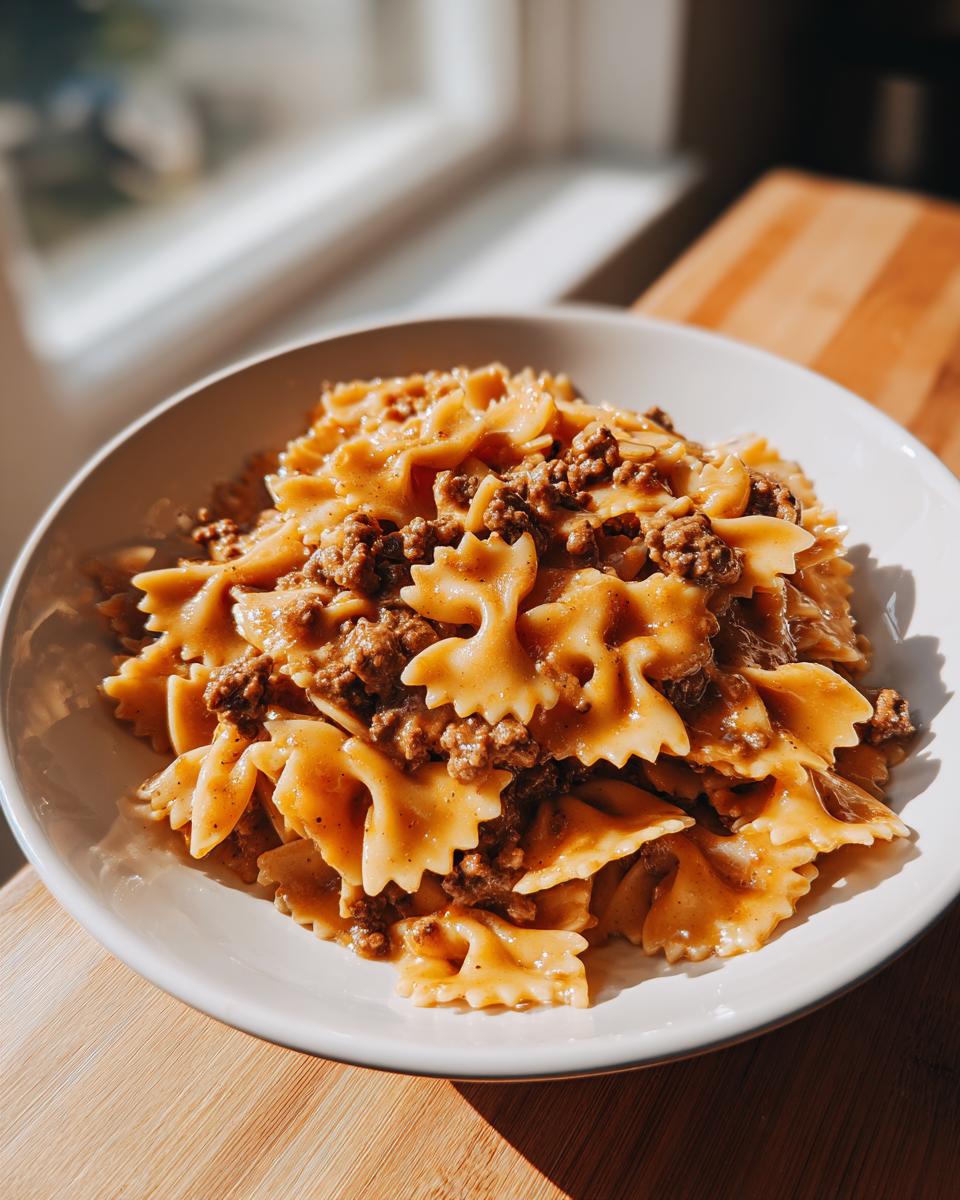 A bowl filled with creamy parmesan garlic beef bowtie pasta, served on a wooden surface near a window.