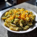 A close-up of creamy pickle pasta salad made with rotini pasta, green relish, and topped with shredded cheddar cheese.