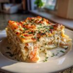 A decadent slice of seafood lasagna with creamy white sauce, visible shrimp, and browned cheese topping.