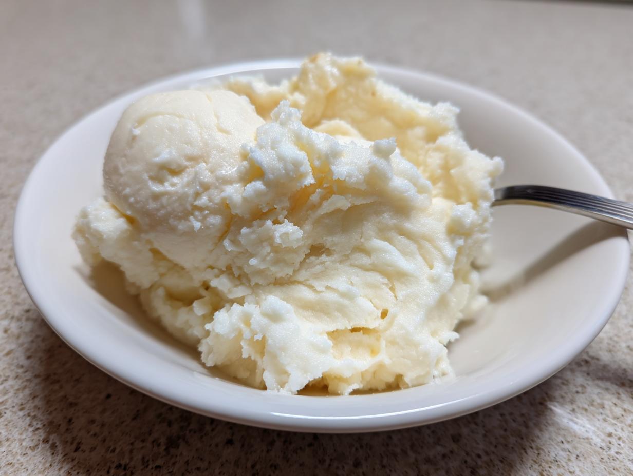 A close-up of creamy, fluffy slow cooker mashed potatoes served in a small white bowl with a spoon.