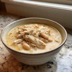 A rustic bowl filled with creamy white chicken chili featuring shredded chicken and white beans.