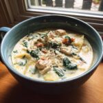 A close-up of a hearty bowl of creamy white chicken lasagna soup with spinach and pasta.