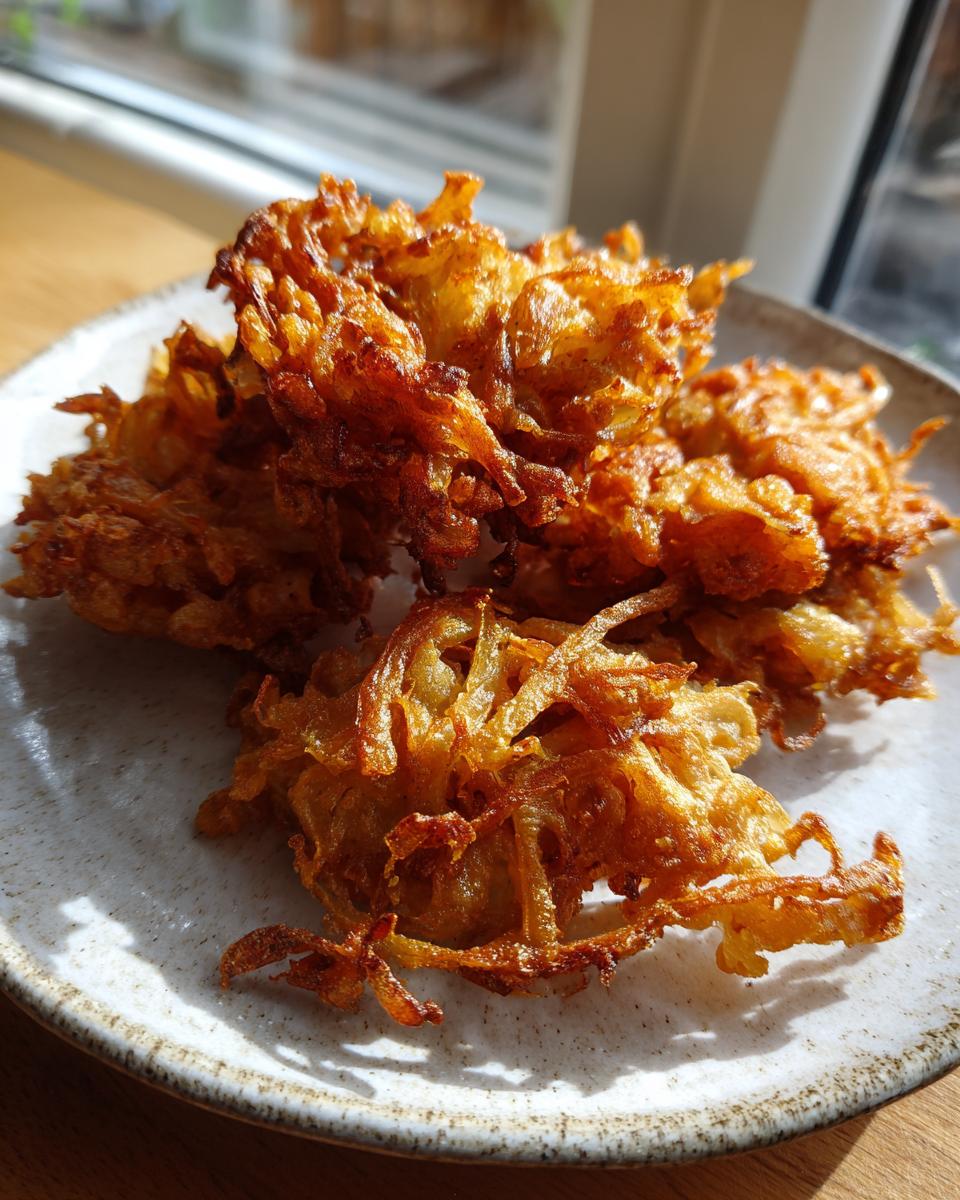 Close-up of several golden-brown, crispy Amish Onion Fritters piled on a light-colored, speckled plate.