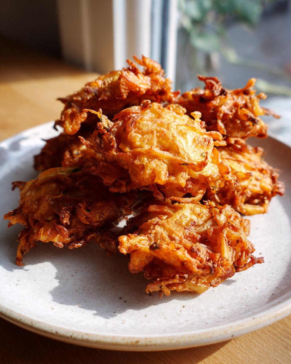 A pile of golden brown, crispy Amish Onion Fritters stacked high on a light-colored, speckled plate.