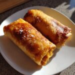 Two golden brown Baked Chicken Chimichangas sprinkled with flaky sea salt on a white plate.