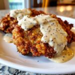 Close-up of crispy, golden brown chicken fried steak smothered in creamy black pepper gravy.