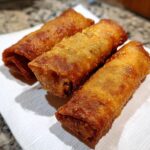 Three perfectly golden brown, crispy fried egg roll appetizers resting on a white paper towel.