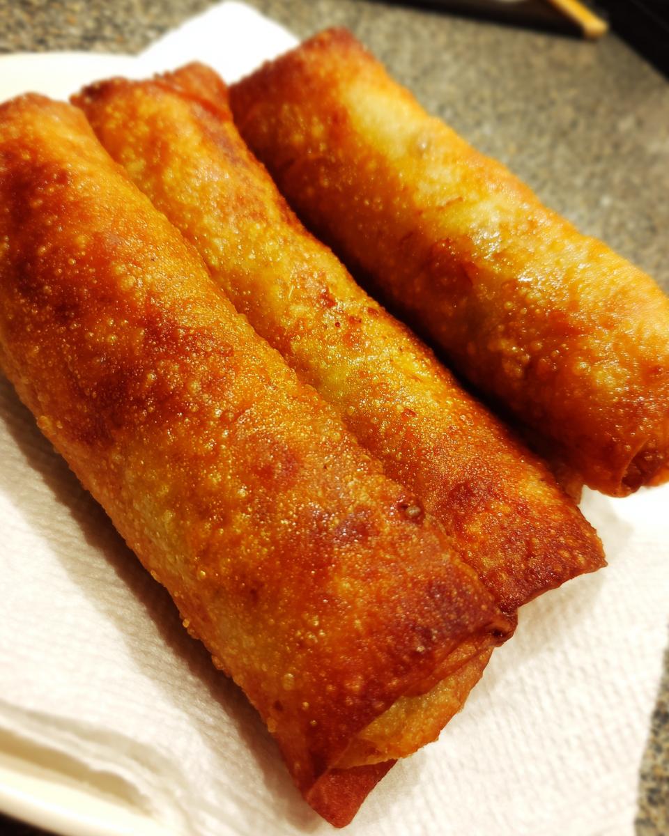 Three perfectly golden brown, crispy fried egg roll appetizers resting on a white paper towel.