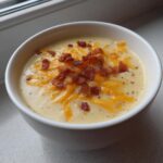 Close-up of a creamy bowl of easy crockpot potato soup topped with shredded cheddar cheese and crispy bacon bits.