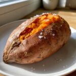 A close-up of a perfectly baked sweet potatoes, split open and sprinkled with large flakes of sea salt.