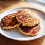 A stack of three fluffy banana oatmeal pancakes with golden brown, textured tops served on a white plate.